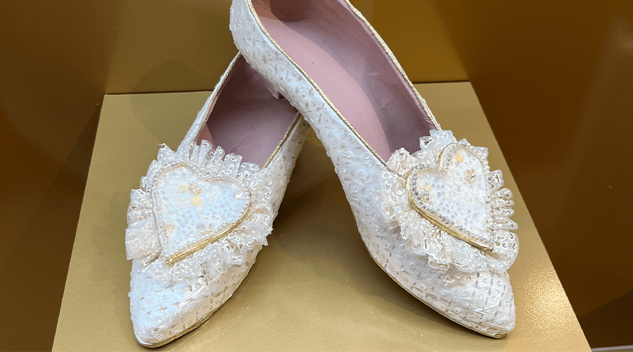 A pair of Princess Diana's white shoes on display at the Princess Diana & The Royals Exhibition in Las Vegas  sitting on a gold box in a glass casing with pink insoles. 