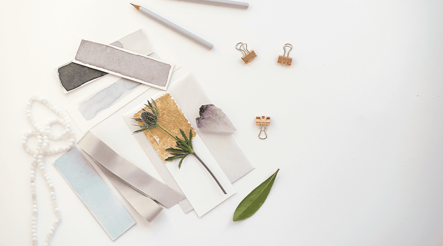 A selection of ribbons, dried flowers, pencils and packaging elements on top of a white counter for wedding guest hampers.