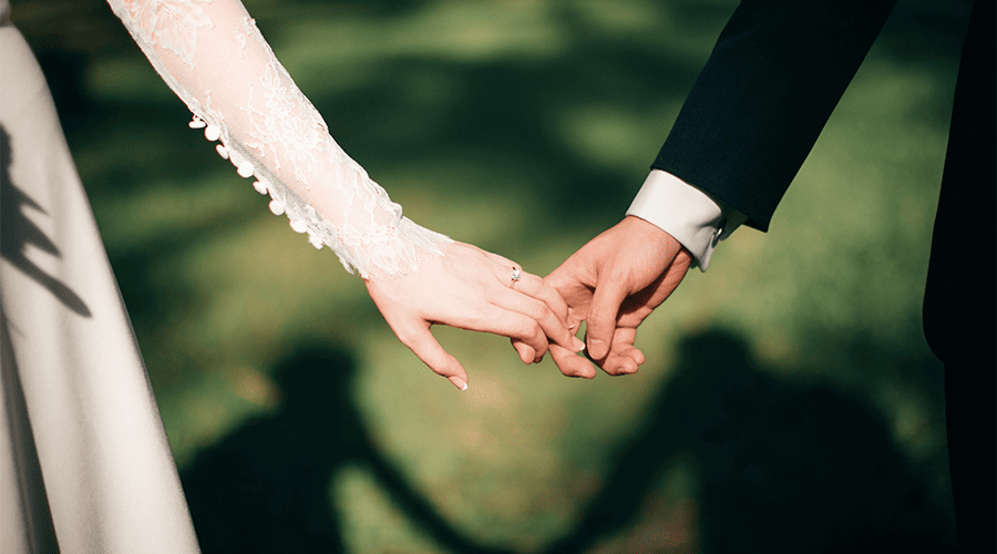 A bride and groom holding hands on their wedding day with their shadow in the background against a green lawn.