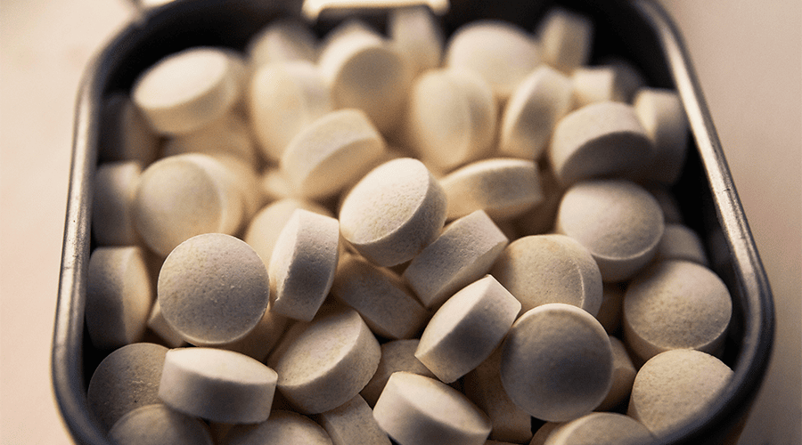 A selection of white breath mints in a grey/black open tin as part of a wedding day emergency kit against an off-white backdrop. 