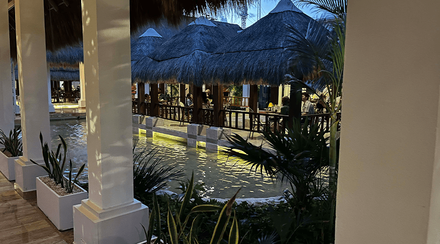 An open-air restaurant dining area at Dreams Sapphire Resort Mexico with thatched roof palapa, water feature view, and no air conditioning at the all-inclusive resort.